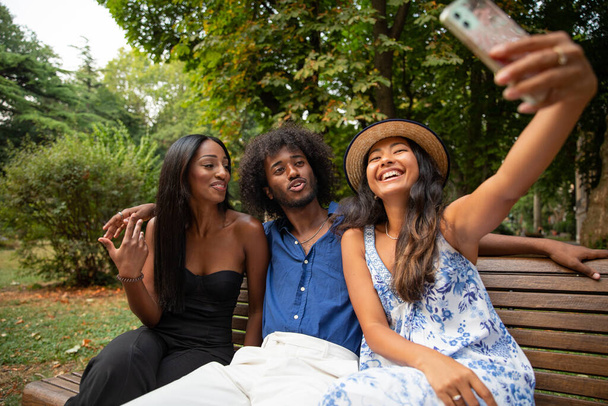 Three friends at the park take a selfie and smile happily, people of different ethnicities together - Фото, изображение