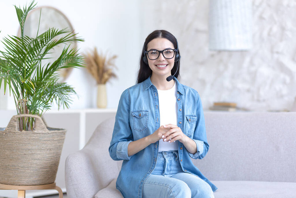 Portrait of a young beautiful woman at home, using a headset for a video call, smiling and looking at the camera - Foto, Bild