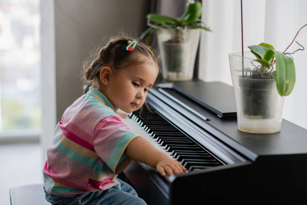 Müzik okulunda piyano çalan tatlı küçük bir kız. Anaokulu çocuğu müzik aleti çalmayı öğreniyor. - Fotoğraf, Görsel