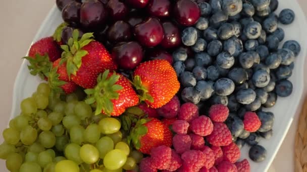 Tuoreita mehukkaita marjoja ja hedelmiä lautasella. Mustikoiden, mansikoiden, kirsikoiden, viinirypäleiden kierto, lähikuva - Materiaali, video