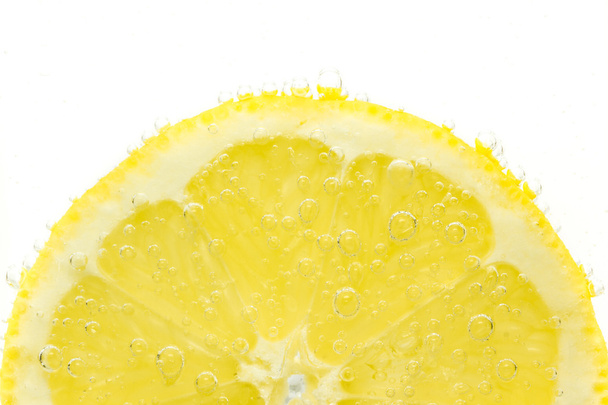 Fresh lemon in soda water covered with bubbles on white background - Photo, Image