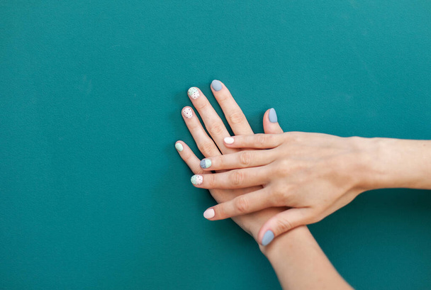 Beautiful female hands with pastel color manicure on green background - 写真・画像