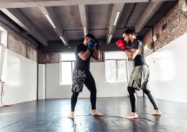Zwei Sparringspartner eines Kickboxers in Boxhandschuhen üben Kicks in einer Sporthalle - Foto, Bild