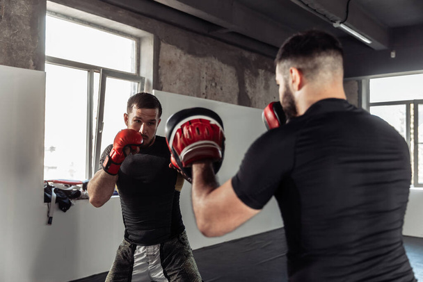Male fighter trains punches with partner with training boxing paws - Photo, Image
