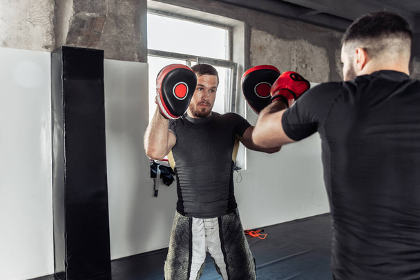 Male fighter trains punches with partner with training boxing paws - Φωτογραφία, εικόνα