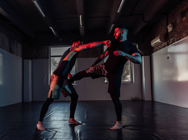 MMA strijders trainen trappen en verdediging in neon licht in sporthal - Foto, afbeelding