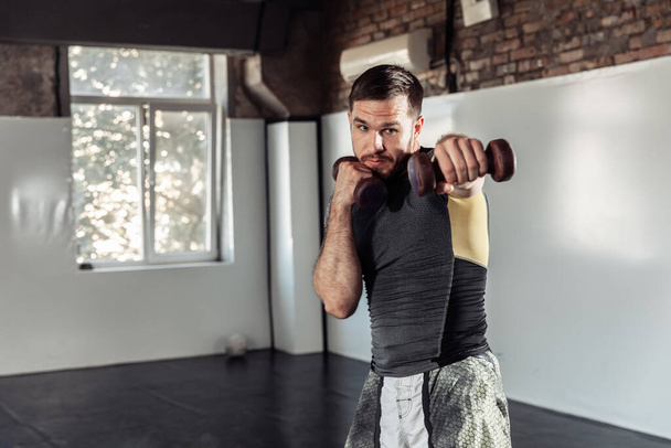 Спортивный боец тренирует удары гантелями в спортзале - Фото, изображение