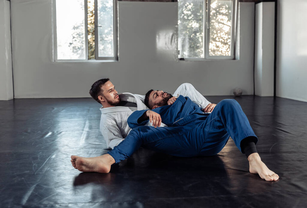Deux combattants en train d'entraîner un partenaire dans un kimono s'entraînent dans une salle de sport - Photo, image