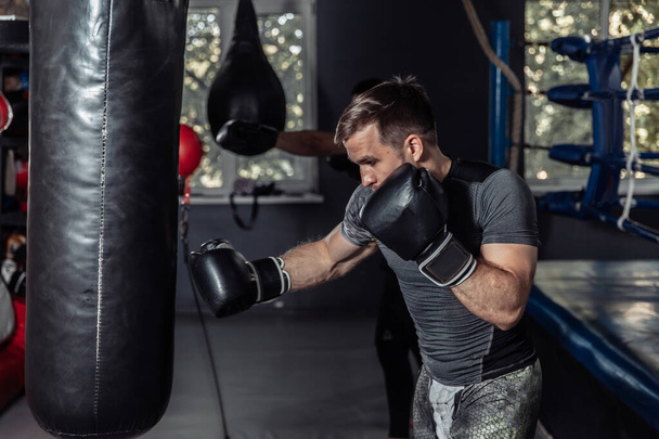 Athlete boxer trains punches in boxing gloves with a punching bag - Foto, Imagen