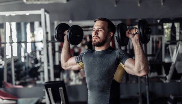 Athletic man exercising shoulder muscles with dumbbells in his hands - Foto, Bild