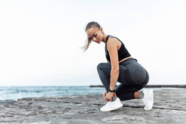 Fit woman tying her shoelaces on urban beach. Healthy lifestyle - 写真・画像