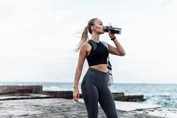 Fit woman drinks water on urban beach. Outdoor workout - Foto, Imagem