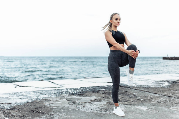 Beautiful young fit woman in sportswear training alone on urban beach. Healthy lifestyle concept - Photo, Image