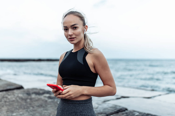Fit woman in sportswear using smartphone on urban beach - Photo, Image