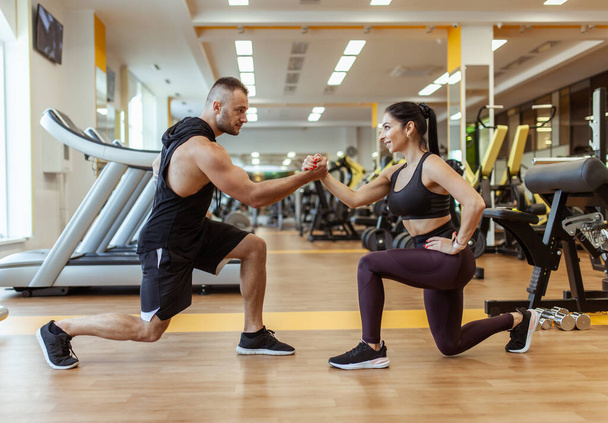 Athletic man with woman doing lunges holding hands in the gym. Workout together - 写真・画像