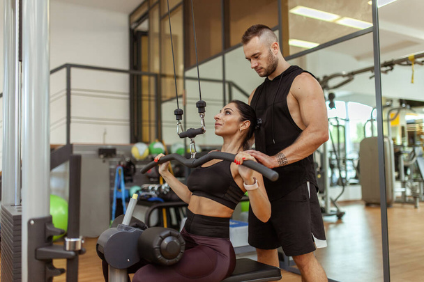 Young fit woman training muscles with personal trainer man in the gym - Foto, afbeelding