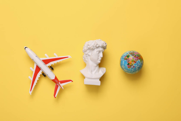 Model airplane and David bust with globe on yellow background. Travel concept. Flat lay, top view - Photo, image