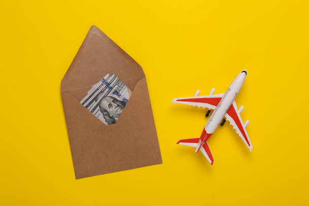Reisconcept. Passagiersvliegtuig en envelop met geld op gele achtergrond. Bovenaanzicht. Vlakke plaat. - Foto, afbeelding