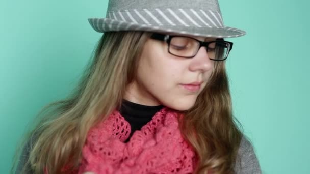Piękna dziewczyna w okularach w kapeluszu na tle muru turkus - Materiał filmowy, wideo