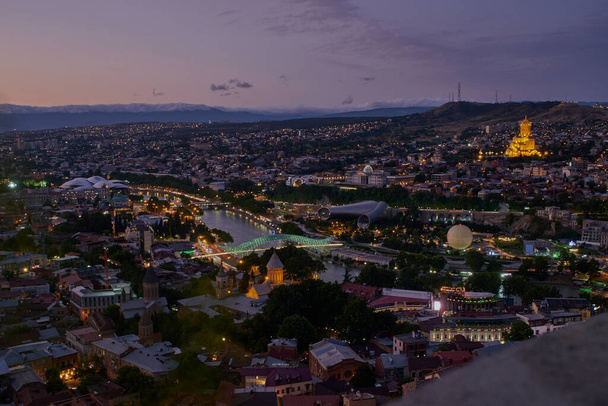 Tbilisi, Georgia night Panoramic view from top of fortress of Narikala showing the bridge of peace, Rike Park, Kura River and Holy Trinity Cathedral of Tbilisi - Photo, image