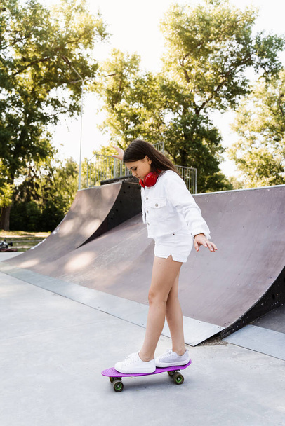 Skater child girl ride on penny board on skate sport ramp at sunset. Sports equipment for kids. Active teenager with pennyboard on skate park playground - Foto, Imagem