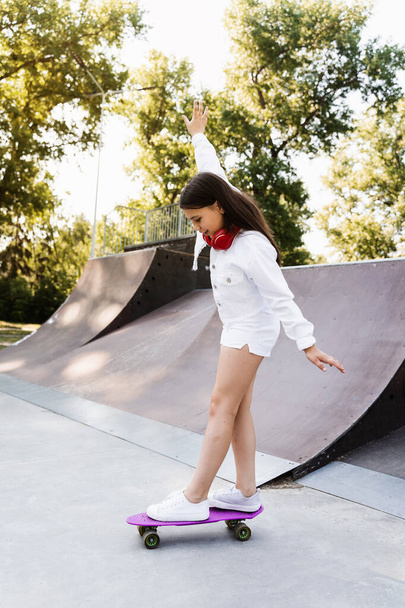 Skater child girl ride on penny board on skate sport ramp at sunset. Sports equipment for kids. Active teenager with pennyboard on skate park playground - Foto, Imagem