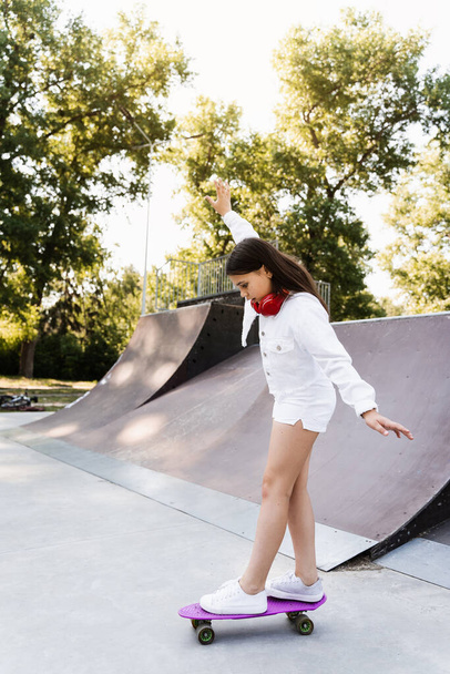 Skater criança menina passeio em penny board em skate esporte rampa ao pôr do sol. Equipamento desportivo para crianças. Adolescente ativo com pennyboard no parque de skate - Foto, Imagem