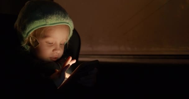 Little girl traveling by car at night. Kid sitting in child safety seat and using smartphone. She is surprised with something on mobile screen - Filmmaterial, Video