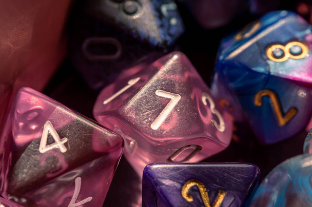 Close-up image of a pink 10-sided die surrounded by various polyhedral dice - Fotó, kép