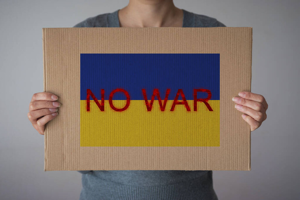 A woman holds sign "NO WAR" with Ukraine flag in front her face - Photo, image