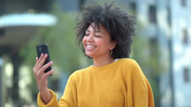 Fun afro student taking selfies on phone for social media and making happy memory in city. Cool, funky and fashionable woman showing peace sign gesture and symbol, blowing kisses and streaming online. - Imágenes, Vídeo