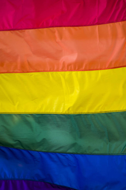 Großaufnahme einer Regenbogenfahne auf einer Straße. Das Symbol der lesbischen bisexuellen Transgender LGBT-Gemeinschaft weht im Wind gegen den bewölkten Himmel. Soziale Bewegung für Freiheit und Gleichheit. Kopierraum  - Foto, Bild