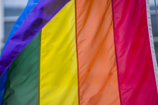Close-Up rainbow gay pride flag outside on a street. Symbol of the Lesbian Bisexual Transgender LGBT community waving in wind against cloudy sky. Social movement for freedom and equliaty. Copy Space  - Photo, Image