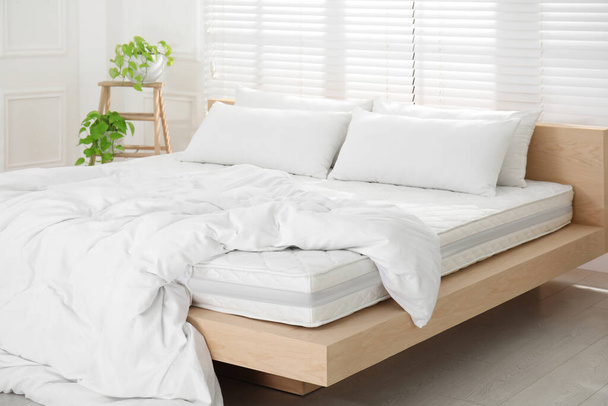 Wooden bed with soft white mattress, blanket and pillows in cozy room interior - Photo, image