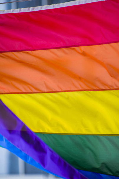 Close-Up rainbow gay pride flag outside on a street. Symbol of the Lesbian Bisexual Transgender LGBT community waving in wind against cloudy sky. Social movement for freedom and equliaty. Copy Space  - Photo, image