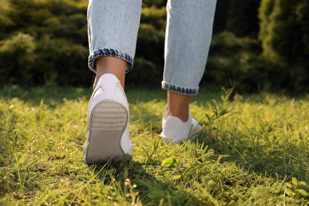 Woman in jeans and white shoes walking on green grass, closeup - Foto, Bild