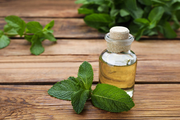 Bottle of essential oil and mint on wooden table, closeup - Foto, afbeelding
