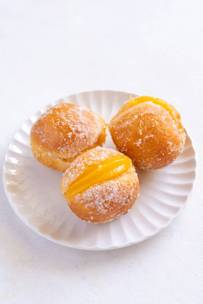 Bola de Berlim, or Berlin Ball, a Portuguese pastry made from a fried doughnut filled with sweet eggy cream on a white plate - Photo, Image