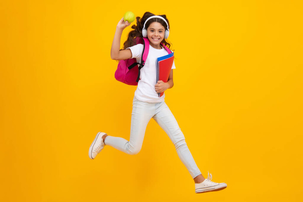 Schoolchild, teenage student girl with headphones and school bag backpack on yellow isolated studio background. Children school and education concept - Zdjęcie, obraz