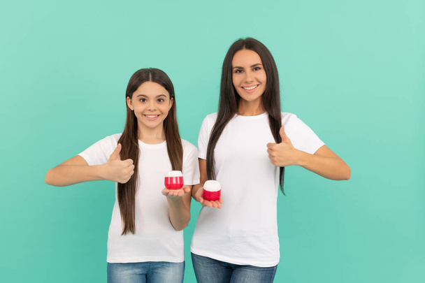 happy mother and daughter hold cream jar on blue background. thumb up. - Foto, Imagem