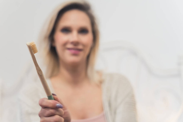 Indoor portrait of an eco bamboo toothbrush held by a blurred unrecognizable blond caucasian woman. Oral healthcare concept. High quality photo - Valokuva, kuva