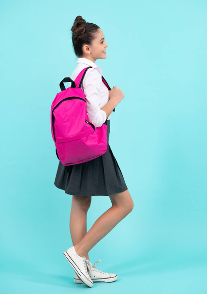 Schoolgirl in school uniform with school bag. Schoolchild, teen student on blue isolated background. Happy teenager, positive and smiling emotions of teen girl - 写真・画像
