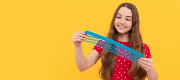 happy kid brushing long hair with comb on yellow background, haircare. Kid girl hair care, horizontal poster. Banner header with copy space - Φωτογραφία, εικόνα