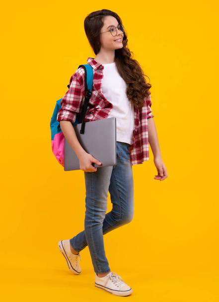 Schoolgirl in school uniform with laptop. Schoolchild, teen student on yellow isolated background. Happy teenager, positive and smiling emotions of teen girl - Photo, Image