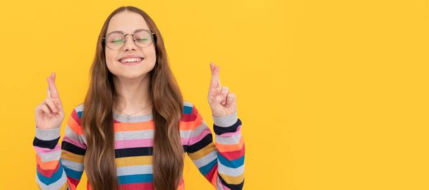 smiling dreamy schoolgirl nerd kid in eyeglasses for vision crossed fingers making wish, dream. Child face, horizontal poster, teenager girl isolated portrait, banner with copy space - Photo, image