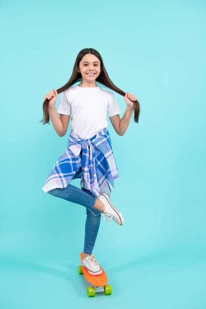 Tiener schoolmeisje met skateboard op studio geïsoleerde achtergrond. Schoolmeisje lente trend, stedelijke tiener stijl. gelukkig tiener, positieve en lachende emoties van tiener meisje - Foto, afbeelding