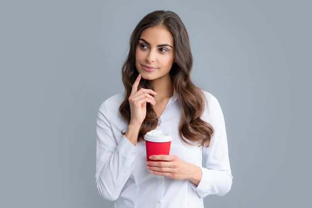 Detailní portrét atraktivní zasněné dívky držící v rukou popíjející latté izolované na šedém pozadí. Mladá brunetka žena pije šálek kávy - Fotografie, Obrázek
