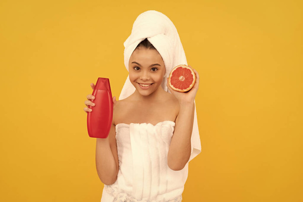 весела дівчина в рушнику з пляшкою шампуню з грейпфрутом на жовтому фоні
. - Фото, зображення