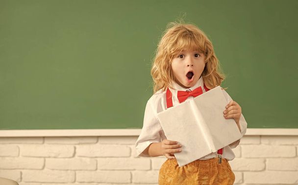 изумленный мальчик в галстуке-бабочке учится в школьном классе с ноутбуком, копировать пространство, вернуться в школу. - Фото, изображение