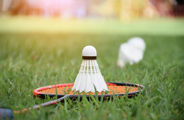 White cream badminton shuttlecock and badminton racket with blurred shuttlecocks on grasslawn background, concept for outdoor badminton playing, soft and selective focus. - Φωτογραφία, εικόνα